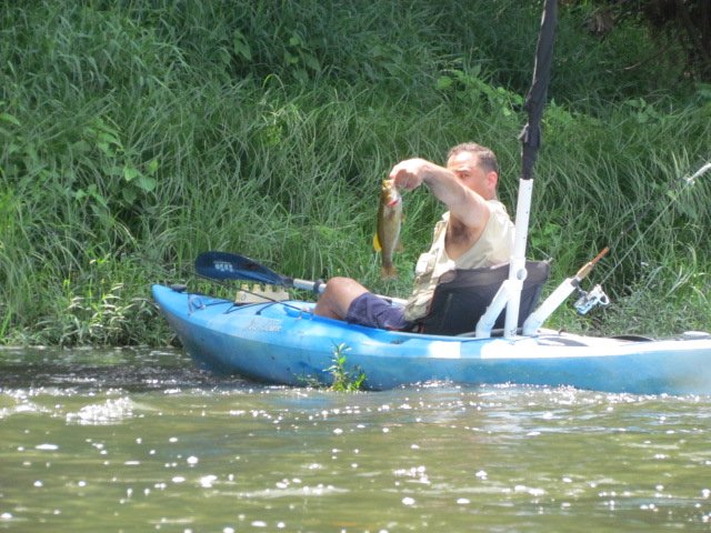 An angler in a kayak holding up a fish on the river.
