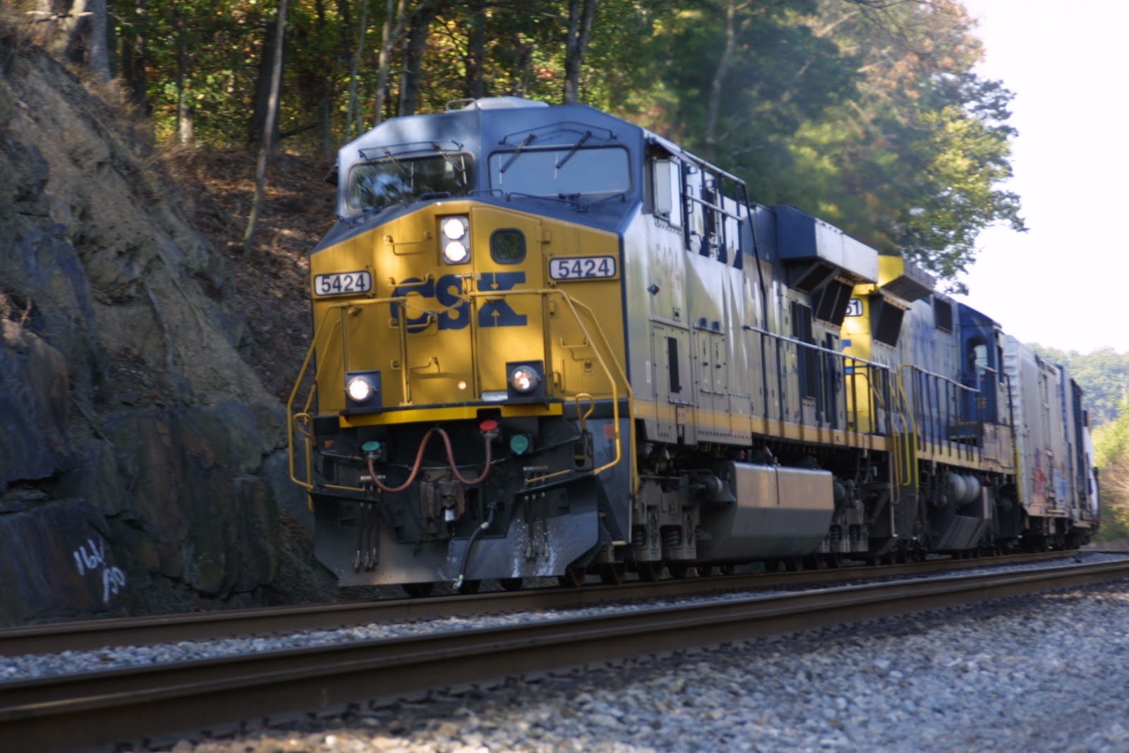 A CSX freight train running the tracks through the mountains, autumn trees around it.