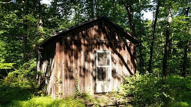 The one-room 1840 schoolhouse, weathered and standing in the woods.