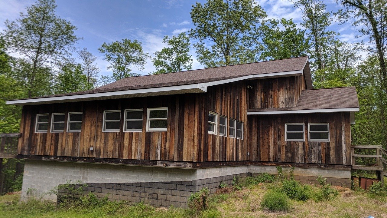 Weathered antique barn siding on the studio building's exterior, set among summer trees.